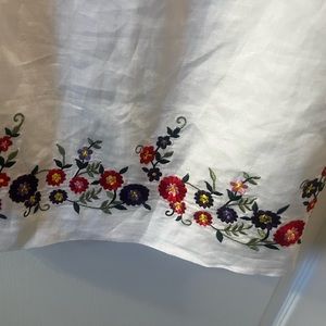 White linen sheath dress with floral embroidered hem.